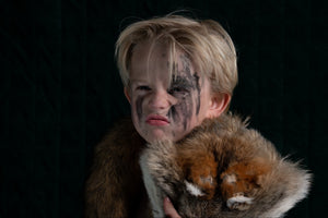 Child with tribal face paint holding a stuffed animal against a black background