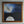 Moonrise painting in an ornate gold frame, showing a white-winged angel holding a golden rope above the moon against a dark blue sky.”