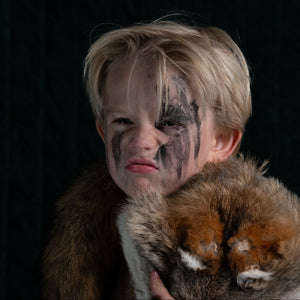 Child with tribal face paint holding a stuffed animal against a black background