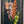 A framed vertical oil painting of gladiolus flowers in shades of orange, pink, and yellow against a dark background, housed in a distressed dark gray frame.