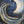 An abstract painting of a crescent moon and swirling waves on a dark blue and black background, accented with gold leaf-like speckles.