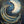 An abstract painting of a crescent moon and swirling waves in deep blue, white, and gold tones, with small gold star-like speckles across a dark navy background.