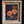 A framed floral painting featuring orange and red poppies in a dark background, housed in an ornate gold frame, displayed against a dark textured wall.