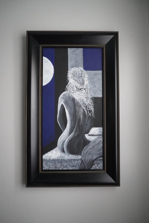 A framed surreal art print featuring a gray stone-like seated figure with long hair against a blue and gray background, enclosed in a black frame and hung on a light gray wall.