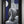 A framed vertical art print featuring a monochrome sculptural figure with a long white beard, set against a dark blue, black, and gray geometric background with a white moon shape. The artwork is housed in a thick black frame with a gold inner border, mounted on a neutral gray wall.