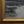 signature “Framed River landscape painting with a small boat near the bank, dark trees, and a pale, cloudy sky.” 