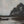 “Framed river landscape painting with a small boat near the bank, dark trees, and a pale, cloudy sky.”