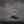 A painted seascape showing a large sailing ship with white sails cutting through dark blue ocean waves under a cloudy gray sky, with small birds in the air.